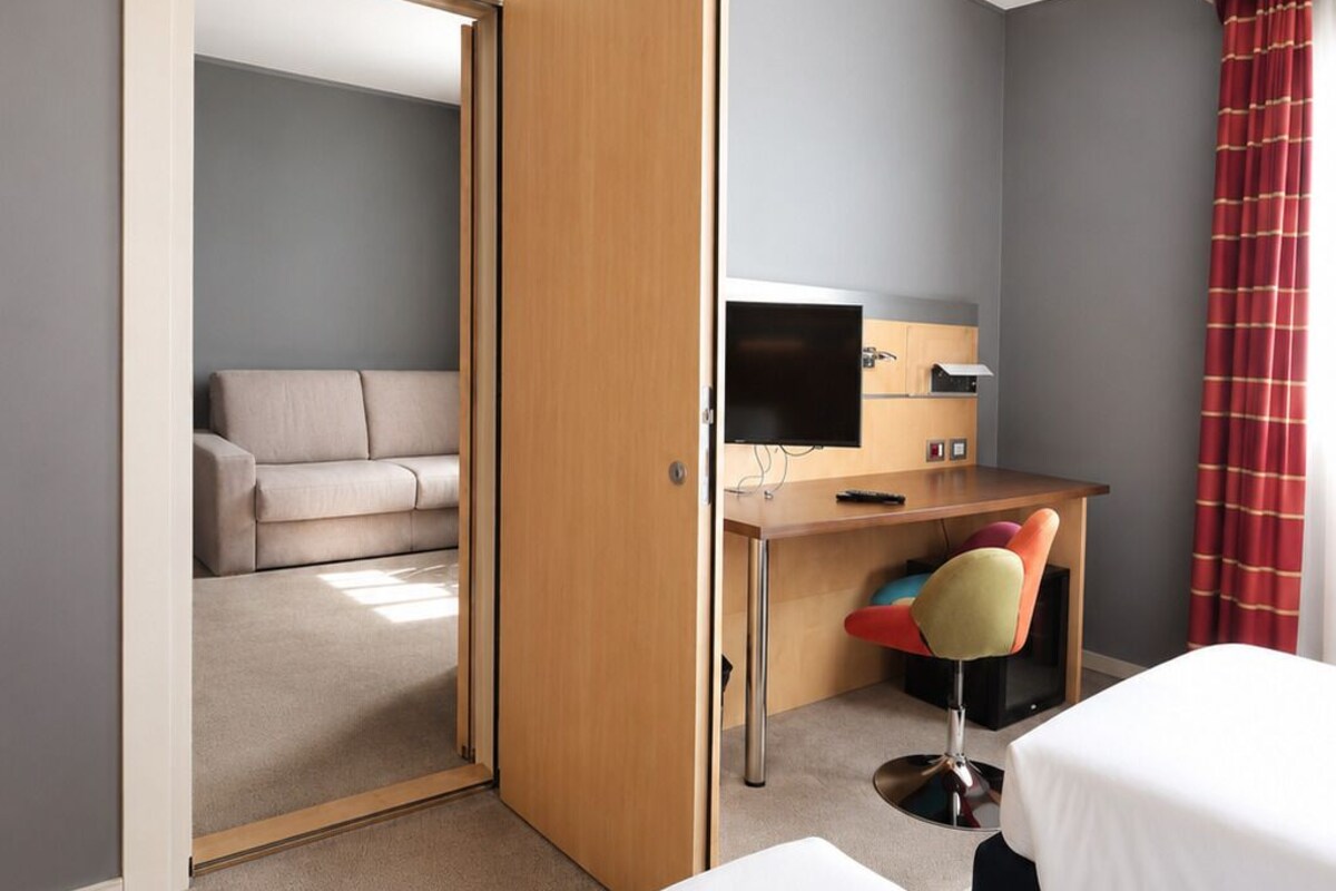 Una habitación de hotel con cama, escritorio, computadora, silla y sofá.