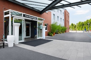 A hotel entrance with a glass door, a sign above it, and a covered walkway. - LVG Hotel Collection - Bergamo West (Mozzo)