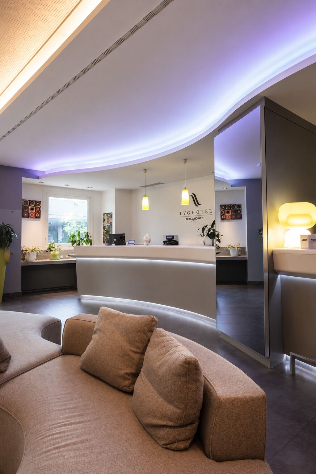 Un hall d’hôtel moderne avec un comptoir d’accueil, un canapé et une grande fenêtre.