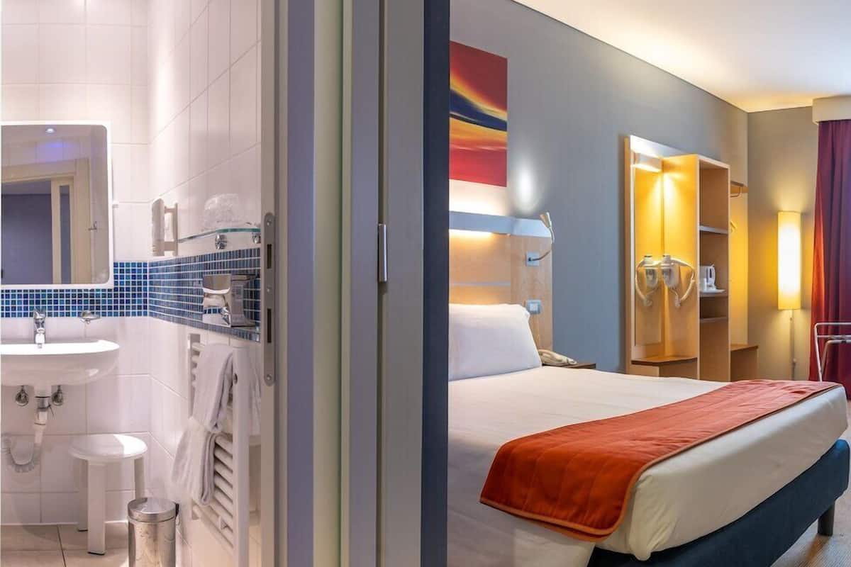 A hotel room with a bed, a bathroom with a sink, and a mirror.