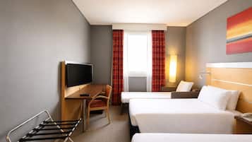 Habitación de hotel con escritorio, dos camas, televisor, lámpara y ventana con cortinas.