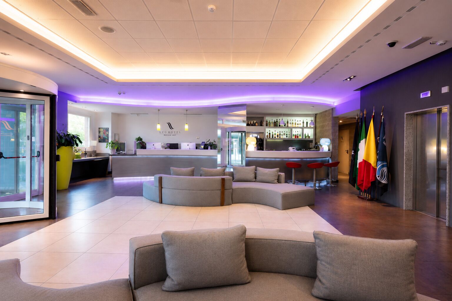 Eine Hotelhalle mit Rezeption, Sitzgelegenheiten, Bar und Flaggen.