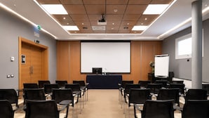 A conference room with a large screen, rows of chairs, a podium, and a wooden panel ceiling. - LVG Hotel Collection - Bergamo West (Mozzo)