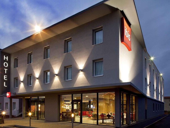 A hotel with a modern facade, multiple windows, and a visible entrance with seating area. - ibis Clermont Ferrand Nord Riom (Riom)