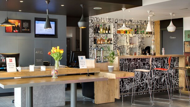 Un espace d’accueil moderne avec un comptoir en bois, un téléviseur et un coin bar agrémenté d’une fresque murale en noir et blanc.