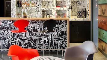 Eine Barbereich mit einem einzigartigen Schwarz-Weiß-Mural, einem roten Stuhl, einem grauen Stuhl und einem kleinen Tisch mit einem Schachbrett.