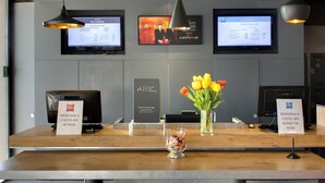 Un comptoir d’accueil d’hôtel doté d’écrans numériques, d’une signalétique indiquant un accueil prioritaire et d’un vase de tulipes.