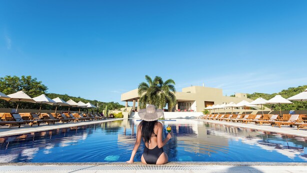 A pool area with lounge chairs, umbrellas, and a building in the background. - Hotel Waya Guajira By OxoHotel (Albania)
