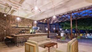A modern bar area with stools, a sofa, and a wooden coffee table. - Hotel Waya Guajira By OxoHotel (Albania)