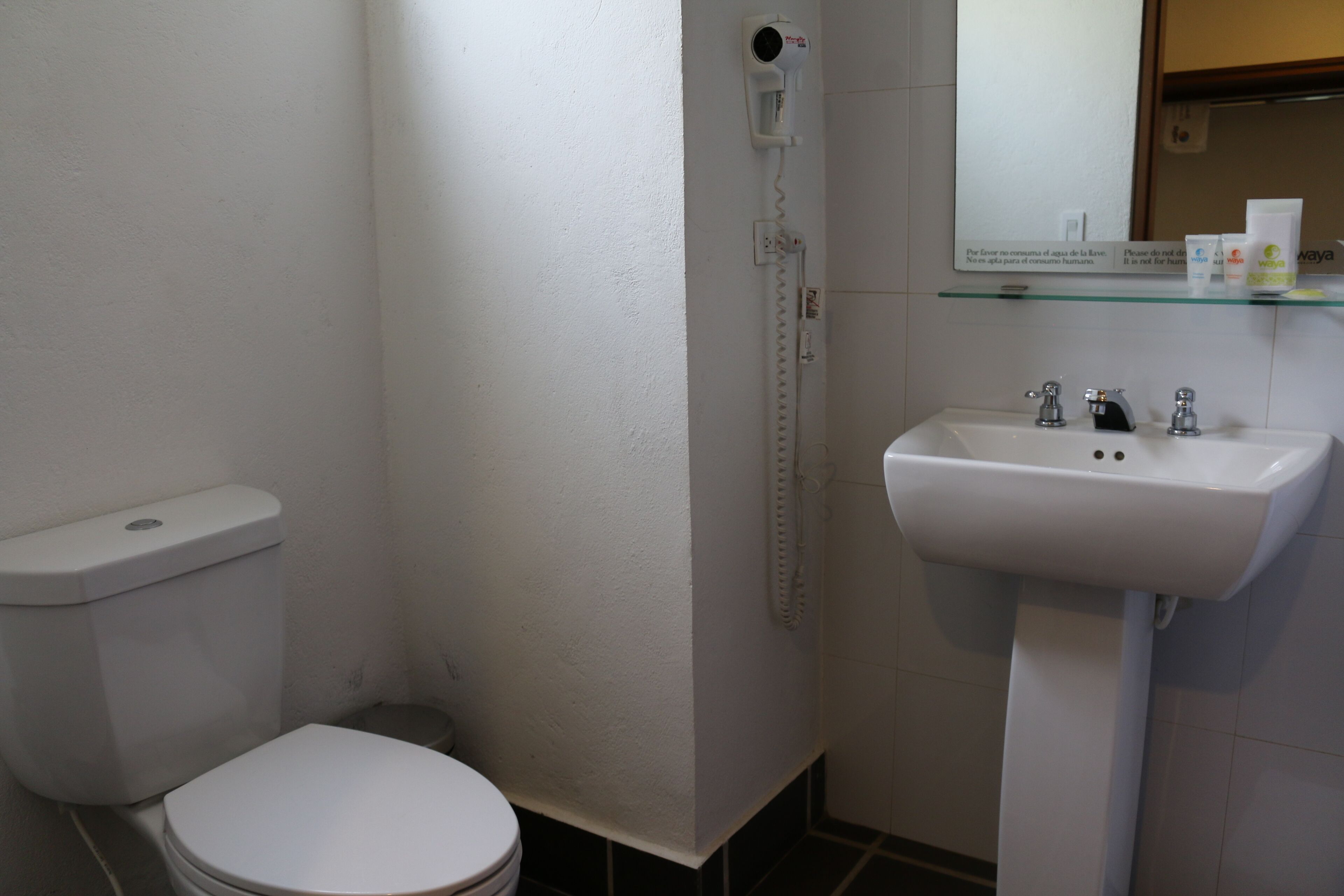 A bathroom with a toilet, a sink, and a hairdryer mounted on the wall.
