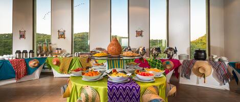 Un buffet proposant une variété de plats et agrémenté d’un grand pot décoratif, le tout mis en valeur par de grandes fenêtres donnant sur un paysage pittoresque.