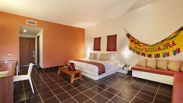Une chambre d’hôtel avec un lit, un canapé, un bureau et une chaise. Un hamac est suspendu au mur.