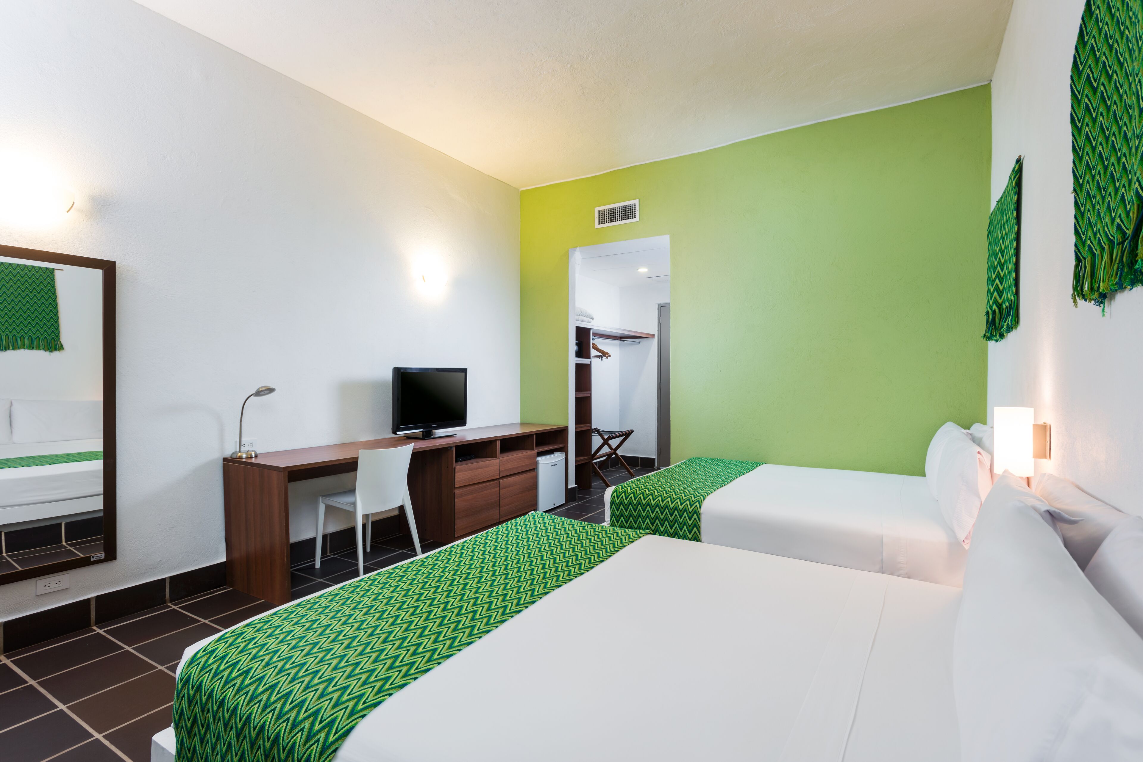A hotel room with two beds, a desk, a chair, and a television.