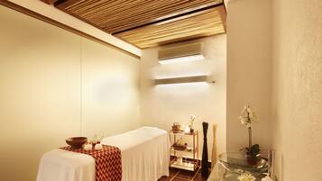Relax in a serene spa room with a massage table, shelf for spa essentials, and a glass table with a vase of flowers.