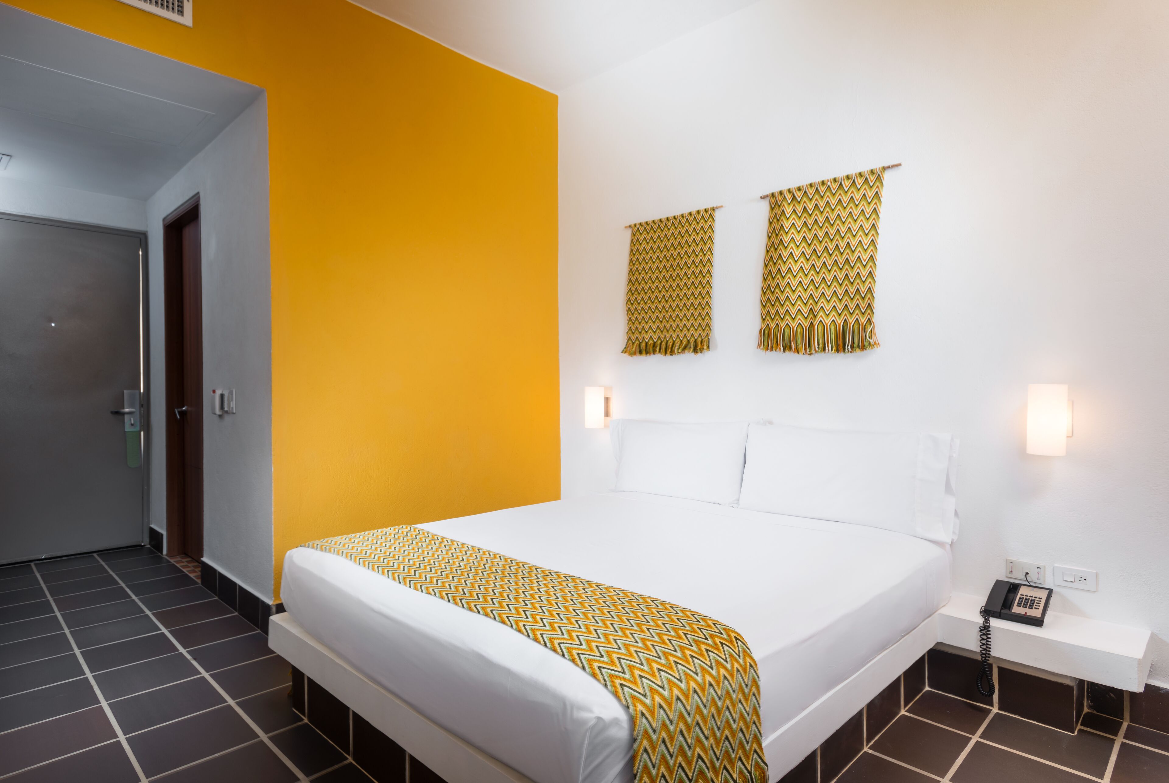 Een hotelkamer met een groot bed, een deur en een muur met twee decoratieve wandtapijten.