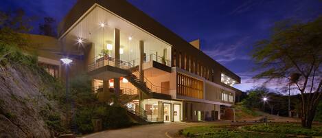 A modern multi-story building with a curved driveway, outdoor lighting, and a landscaped garden.