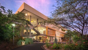 A modern building with a prominent staircase, multiple floors, and a landscaped garden with flowers and trees. - Hotel Waya Guajira By OxoHotel (Albania)