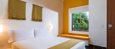 Une chambre d’hôtel avec un grand lit, une fenêtre donnant sur un paysage verdoyant et une porte en bois.