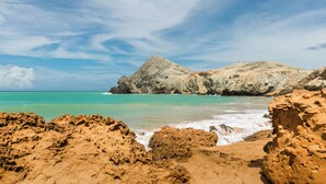 A rocky beach with clear turquoise water and a large rock formation in the background. - Hotel Waya Guajira By OxoHotel (Albania)