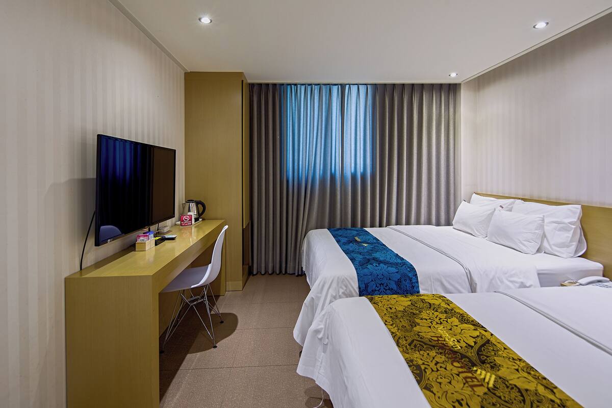 Habitación de hotel con cama, escritorio, silla, televisor y ventana con cortinas.