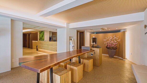 A modern reception area with a wooden reception desk, a potted plant, and a wooden wall panel. - Namsan Hill Hotel (Seoul)