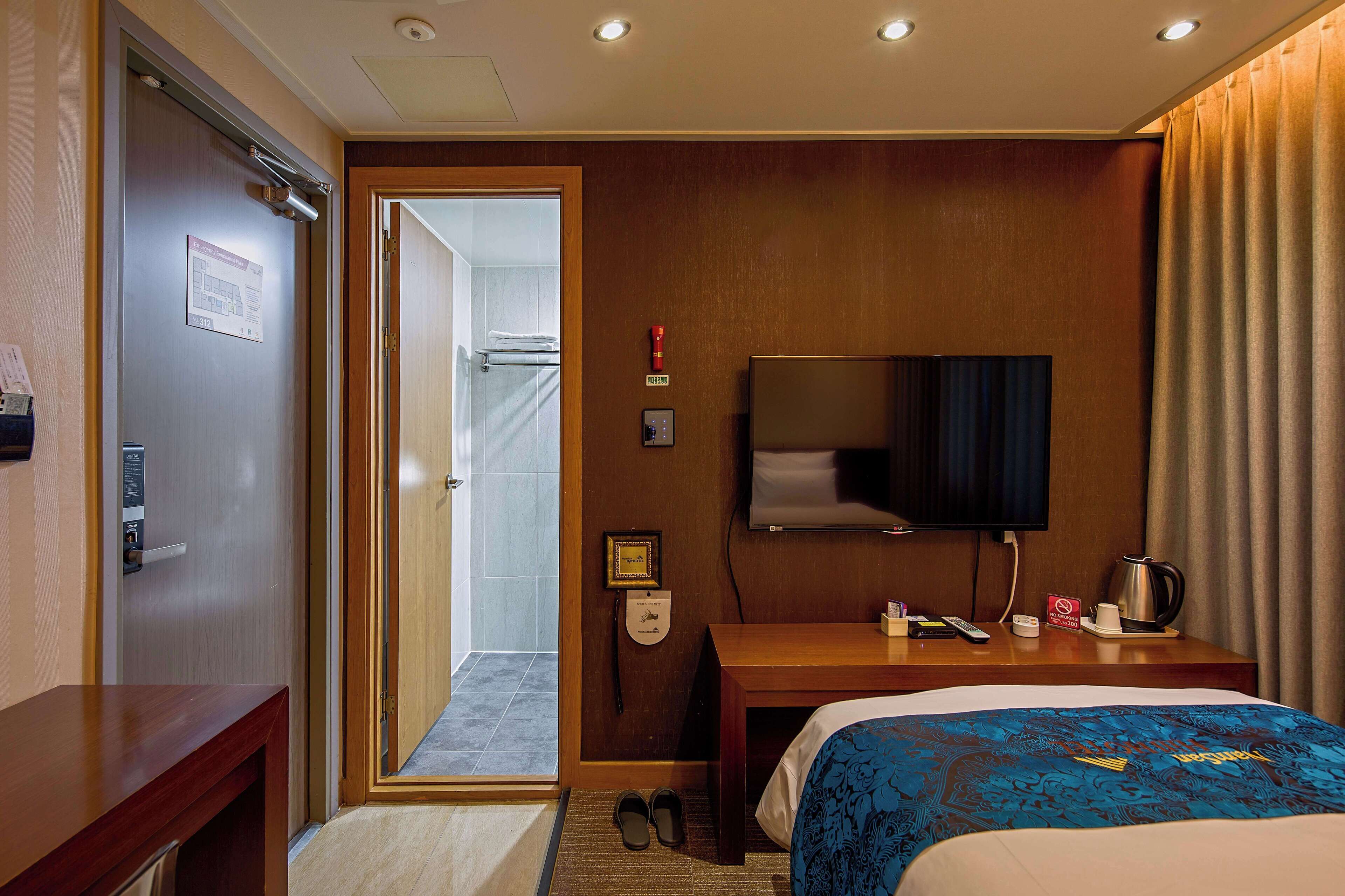 A hotel room with a bed, a desk, a television, and a shower area.