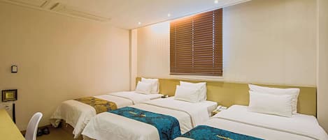 Ein Hotelzimmer mit drei Einzelbetten, einem Schreibtisch und einem Stuhl.