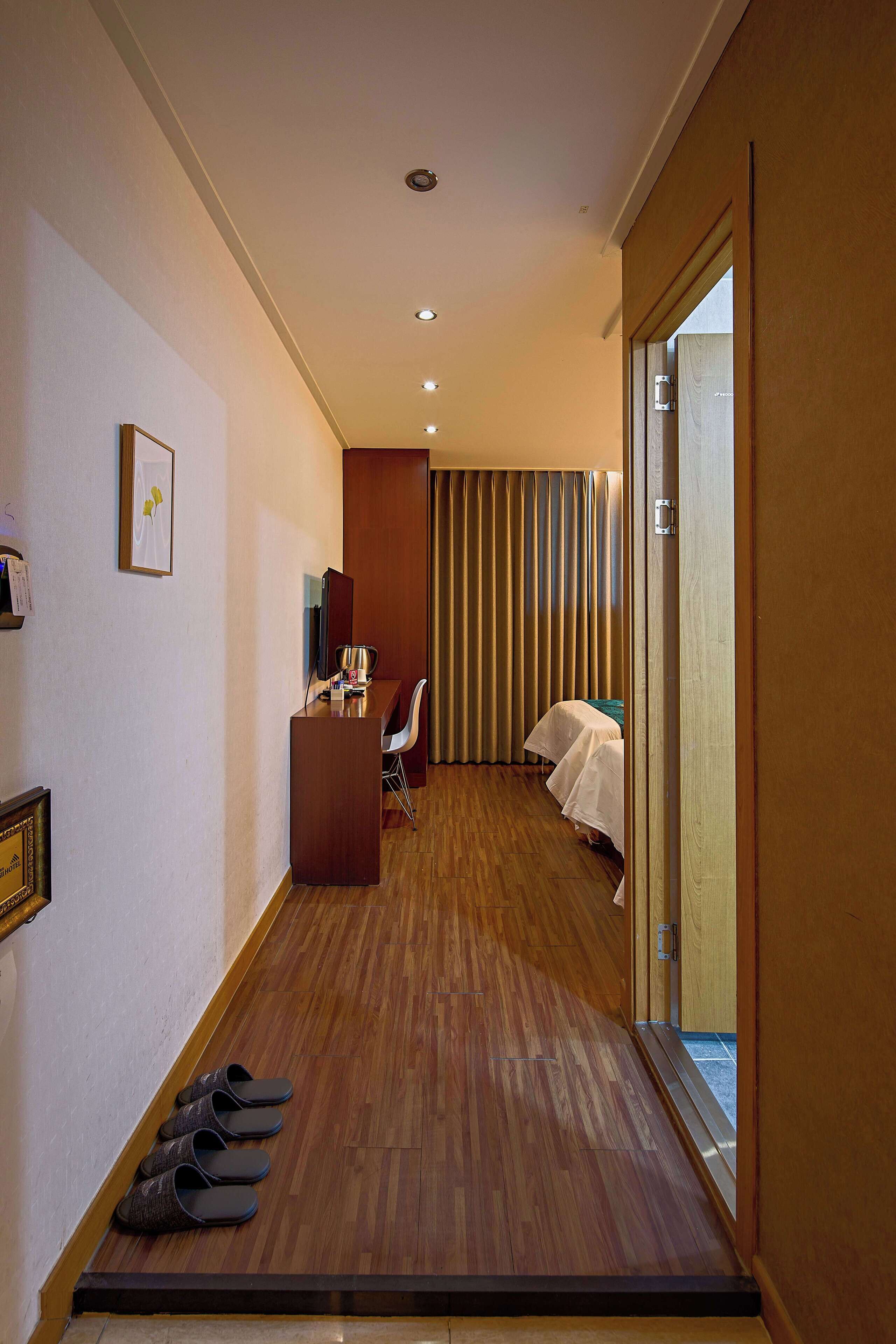 Ein Hotelkorridor mit Holzboden, einem Empfangsbereich, einem Bett mit weißer Bettdecke und einer Schiebetür zu einem Zimmer.