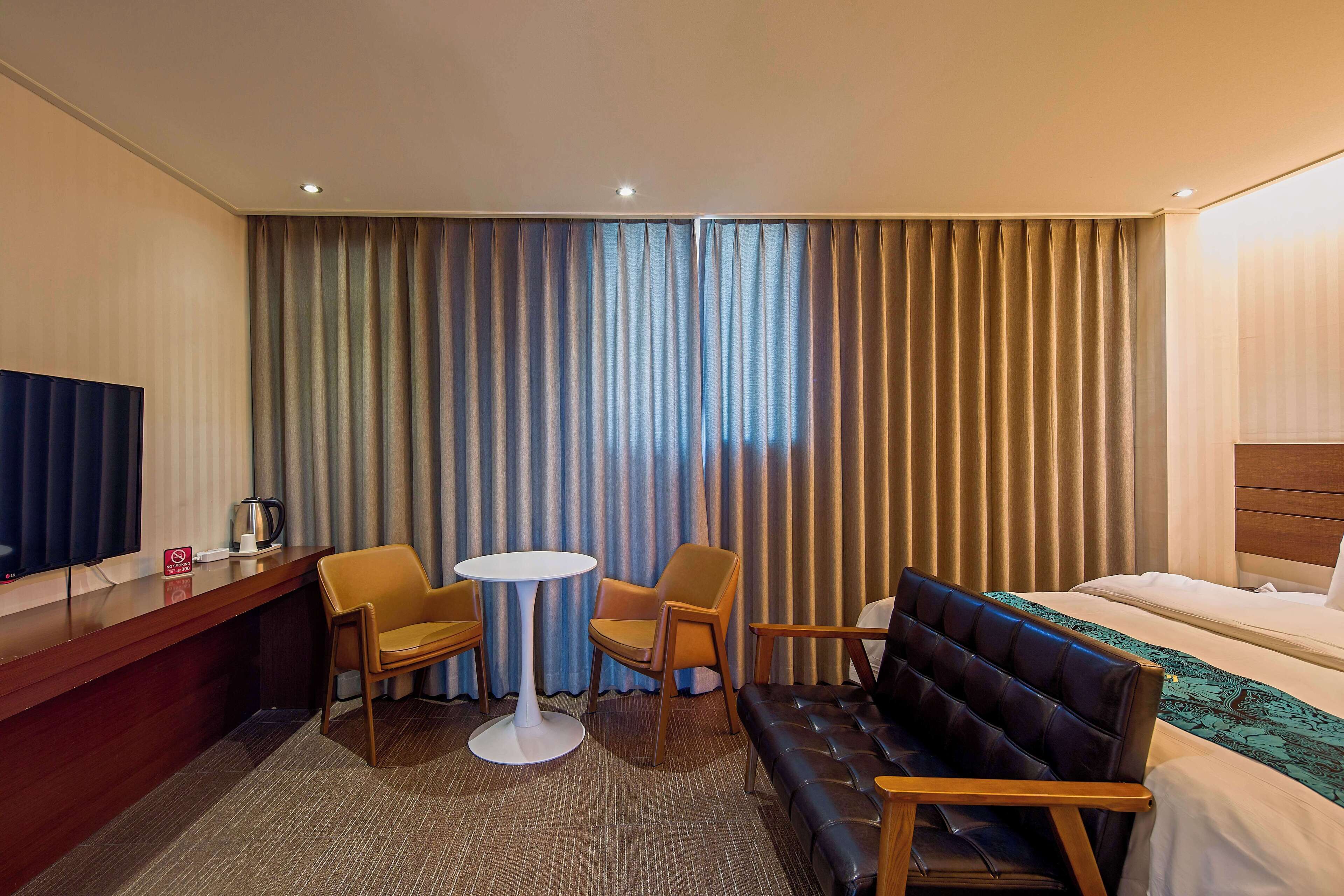 A hotel room with a bed, a sofa, a small table, two chairs, a TV, and a coffee maker.