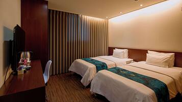 A hotel room with two beds, a desk, a chair, and a television.