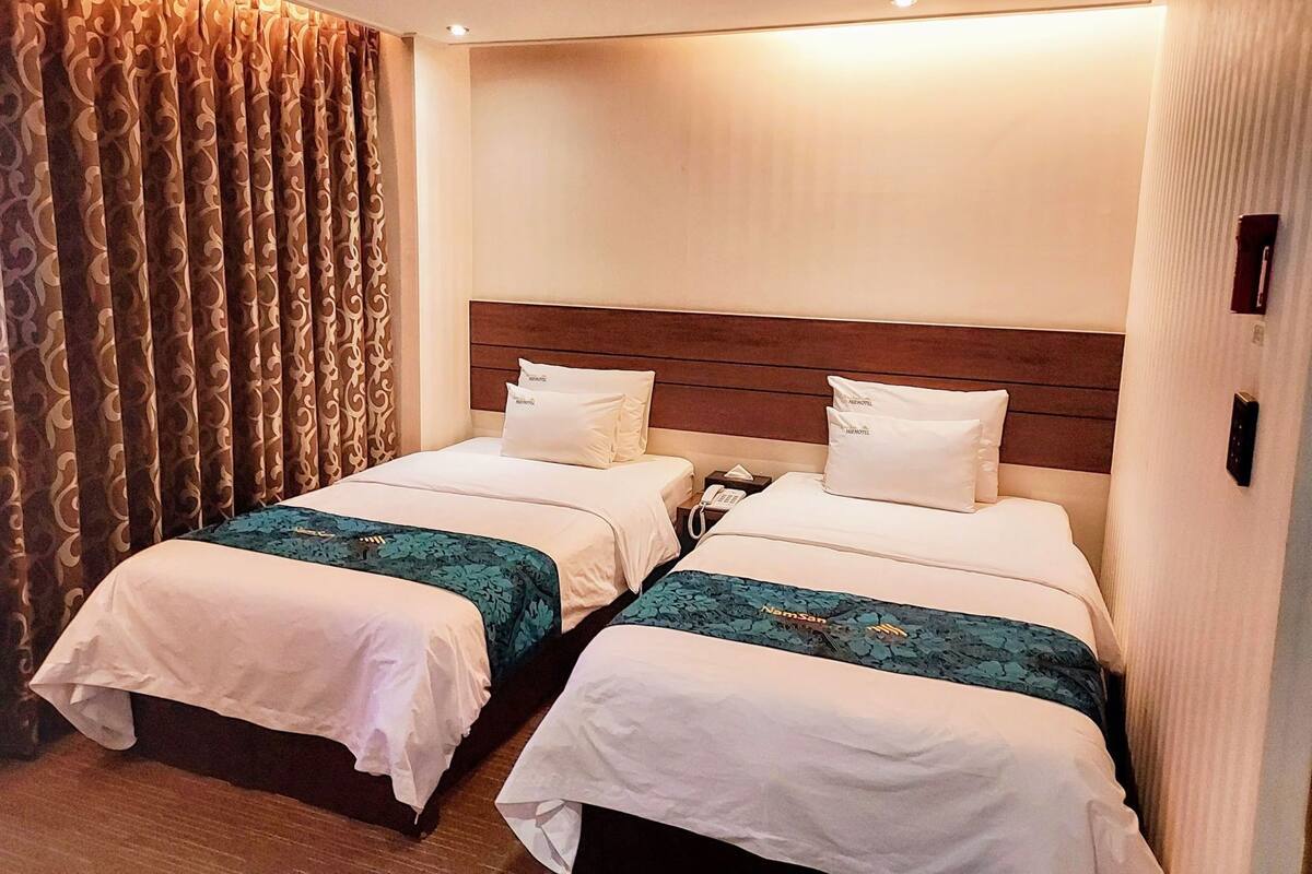 Habitación de hotel con dos camas, cabecero de madera, teléfono y cortina estampada.