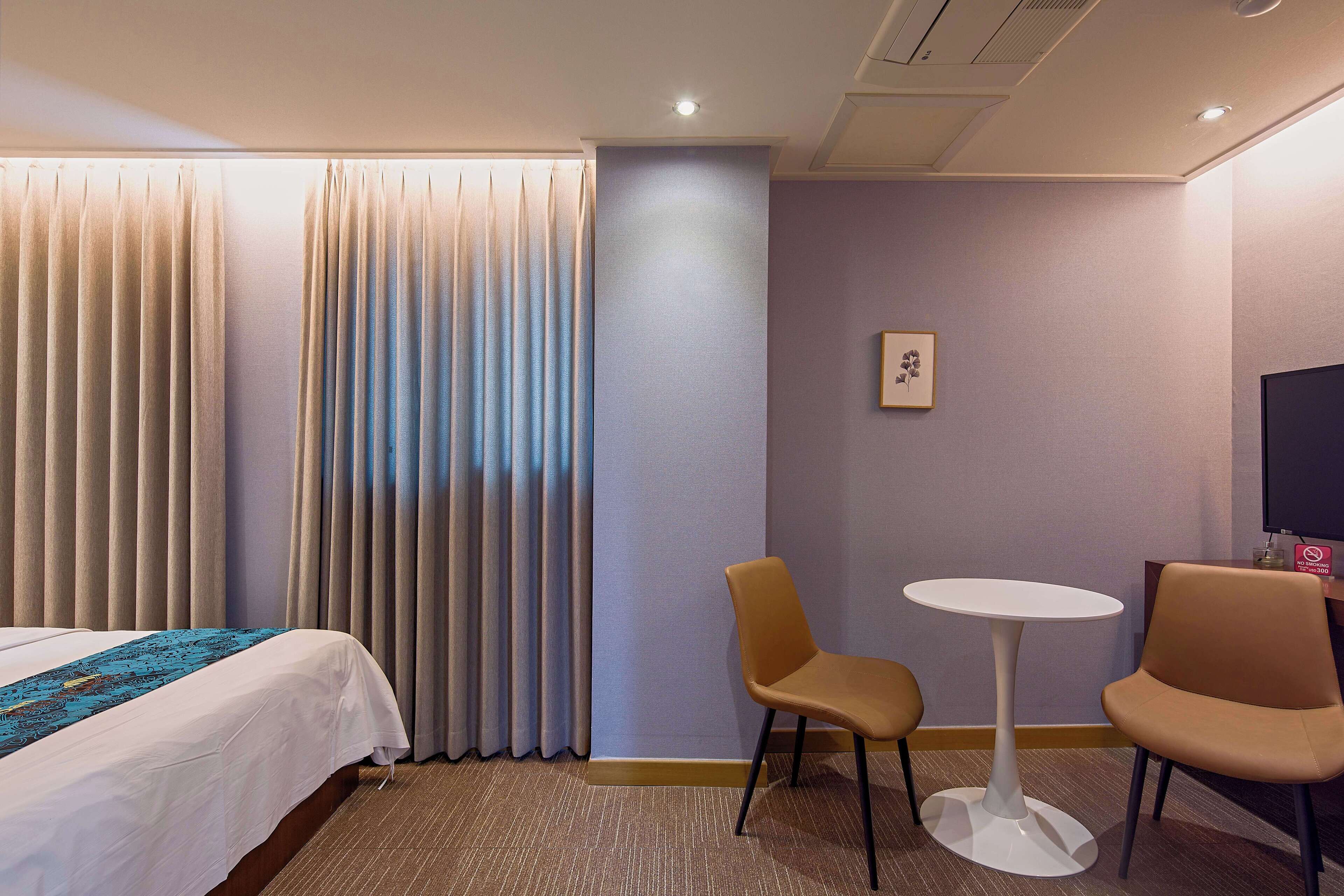 Una habitación de hotel con una cama, dos sillas, una mesita y un televisor.