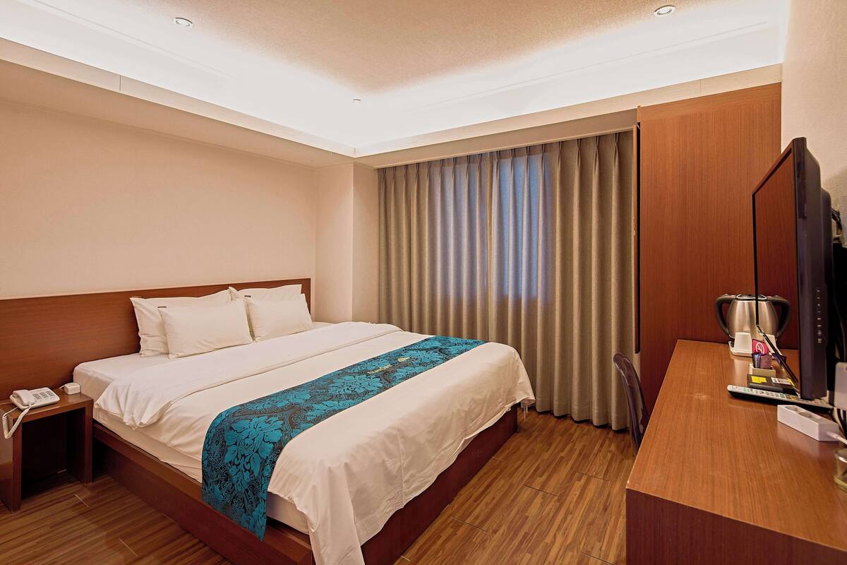 Una habitación de hotel con una cama grande, un escritorio con computadora, un teléfono y una televisión.