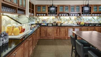 A buffet-style breakfast area with wooden cabinets, a glass display case, and a variety of food items.
