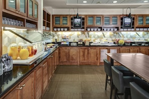 Zona para desayuno tipo buffet con armarios de madera, una vitrina de vidrio y una variedad de alimentos.