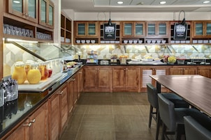 Zona para desayuno tipo buffet con armarios de madera, una vitrina de vidrio y una variedad de alimentos.