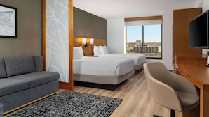 A hotel room with two beds, a sofa, a desk, and a TV.