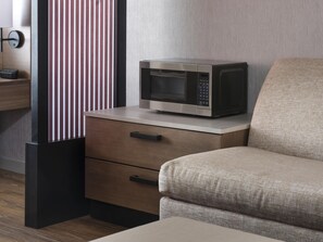 A modern kitchen area with a microwave on a countertop, a wooden drawer, and a striped vertical panel. - Hyatt Place Omaha Downtown Old Market (Omaha)