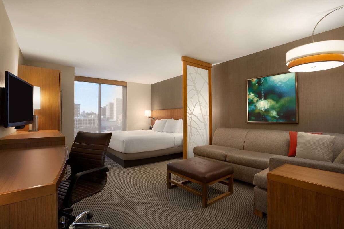 Een hotelkamer met een bed, een bank, een bureau, een televisie, een raam en een schilderij aan de muur.