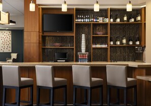 A bar area with a flat-screen TV, shelves of liquor bottles, and bar stools. - Hyatt Place Omaha Downtown Old Market (Omaha)