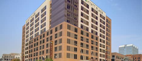 A multi-story hotel with a prominent "Hyatt Place" sign, featuring a modern architectural design with a mix of brick and glass facades.