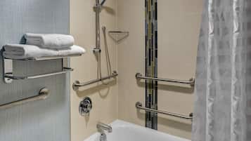 A bathroom with a white bathtub, a towel rack with folded towels, a shower with a handheld showerhead, and a grab bar.