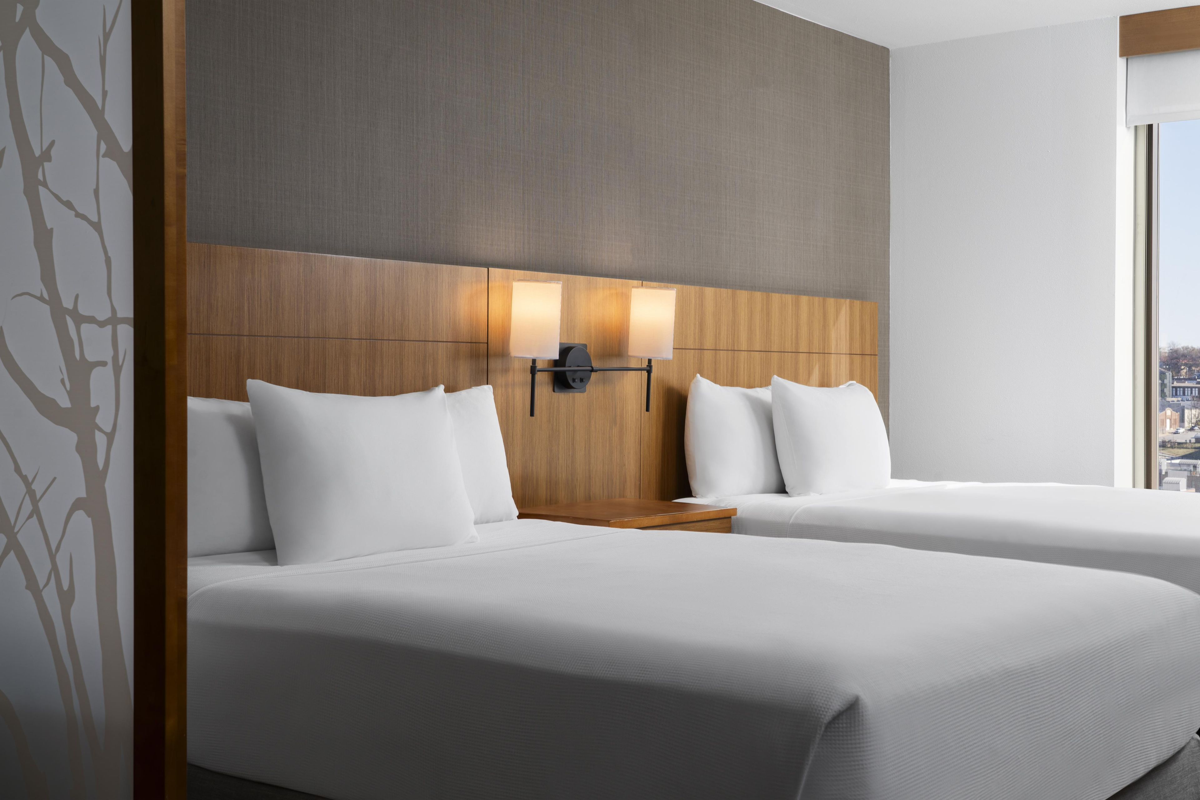 A hotel room with two beds, a wooden headboard, and a city view.