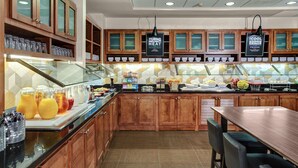 A modern kitchen with wooden cabinets, a glass display case, and a buffet area with various food items.