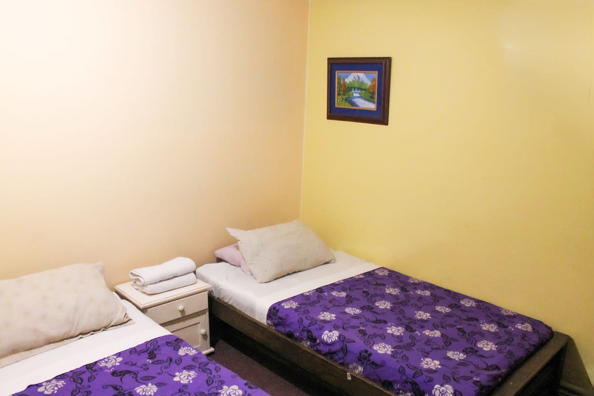 A small, single-room hotel room with two beds, a nightstand, and a framed picture on the wall.