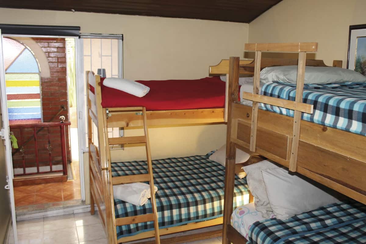 A bunk bed room with a red mattress on the top bunk and checkered bedding on the lower bunk.