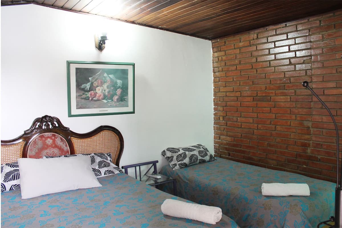 A room with two beds, a wooden ceiling, a brick wall, and a framed picture on the wall.