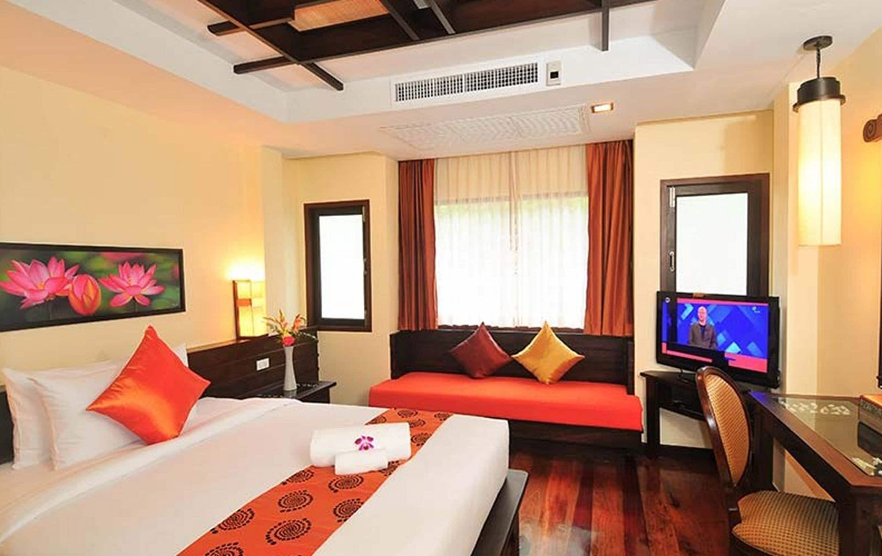 A hotel room with a bed, a desk with a computer, a television, and a window with curtains.