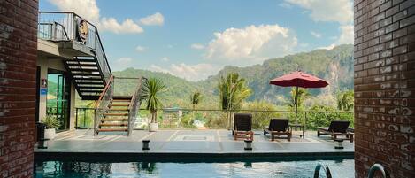 A pool area with a view of mountains, a staircase, and lounge chairs.
