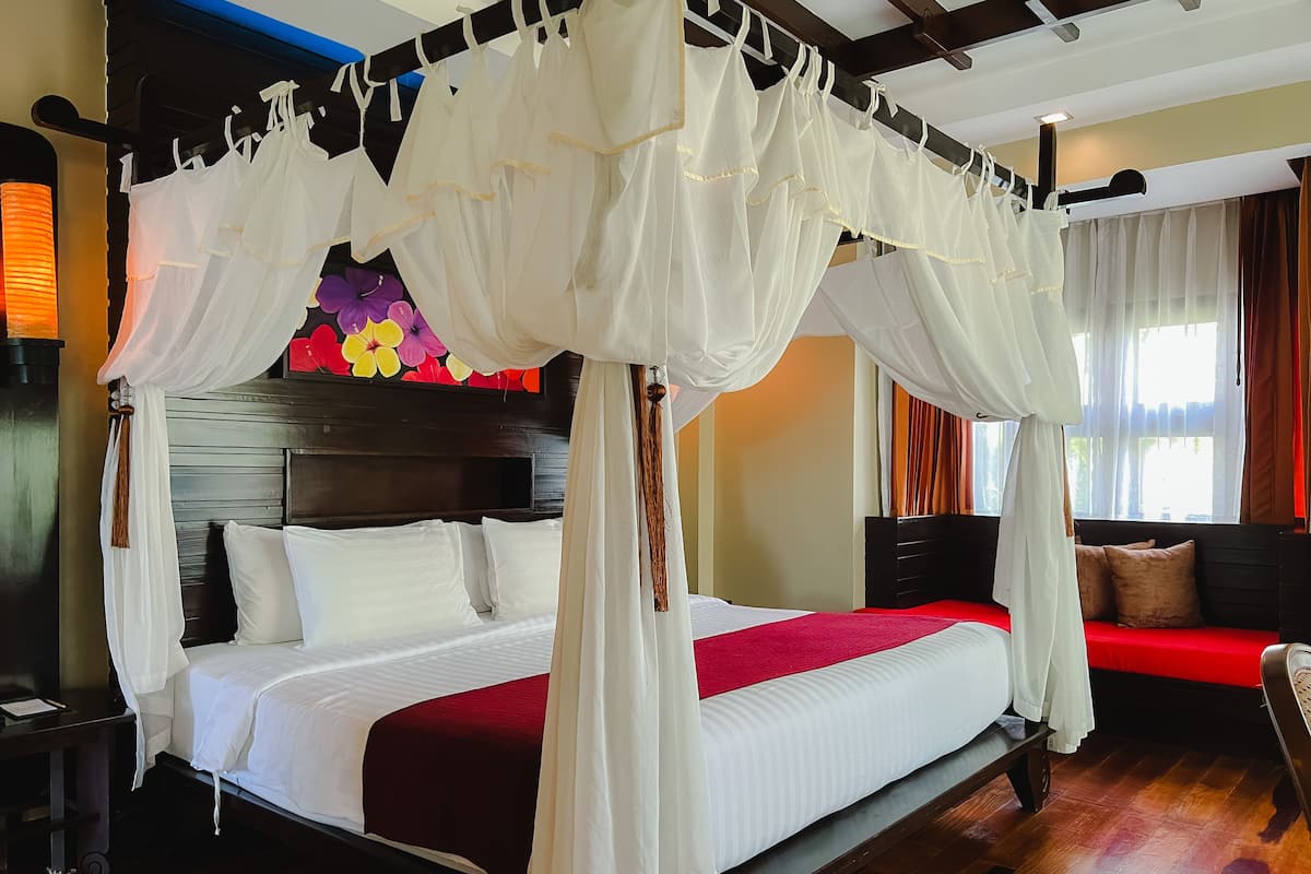 A four-poster canopy bed with white bedding, a wooden headboard, and a red accent pillow.